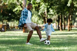 A black man smiling and playing soccer with his son after having ICL.